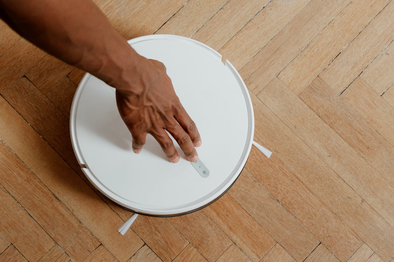 A close-up of a hand activating a robotic vacuum cleaner on a wooden floor.