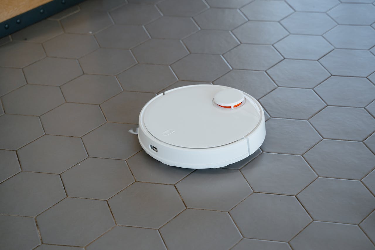 A sleek, white robotic vacuum cleaner operating on a hexagonal tiled floor.